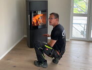 Christoph Kohler kniet neben einem neuen Ofen und erklärt dem neuen Besitzer die SmartControl